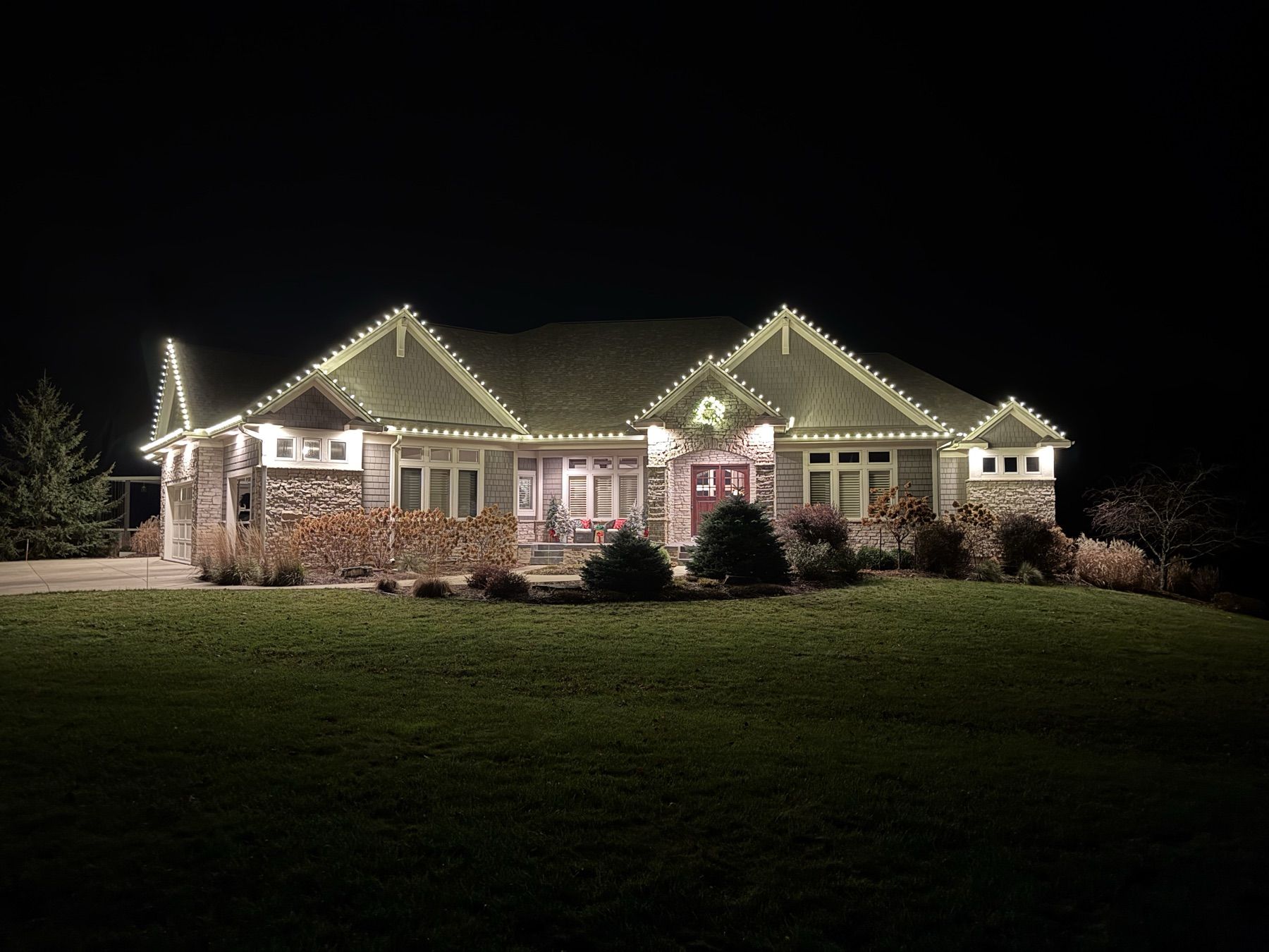 Ranch home with lit rooflines, bushes, and landscaping